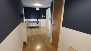 A hallway with wooden flooring, a white cabinet, and a door leading to a room.