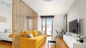 Ein modernes Wohnzimmer mit einem gelben Sofa, einem weißen Schreibtisch, einem Fernseher und einem großen Fenster mit Blick.