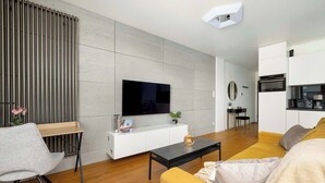 Ein modernes Wohnzimmer mit einem Flachbildfernseher, einem Holztisch, einer Couch und einem Essbereich mit einer Küche im Hintergrund.