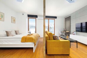A modern bedroom with a bed, a sofa, a TV, and a city view. - Modern Studio | Air Conditioning, Parking and Balcony (Kraków)