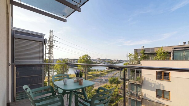Ein Balkon mit Tisch und Stühlen mit Blick auf einen Fluss und Gebäude.