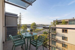 Uma varanda com mesa e cadeiras, com vista para um rio e edifícios.