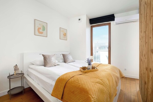 A bedroom with a bed, bedside table, and a window with a view of buildings. - Modern Studio | Air Conditioning, Parking and Balcony (Kraków)
