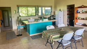 Una cocina compacta con una isla central, un área de comedor con mesa y sillas, y un espacio de almacenamiento con estanterías.