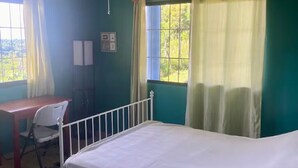 Habitación con cama, escritorio y silla. Hay una ventana con cortinas.