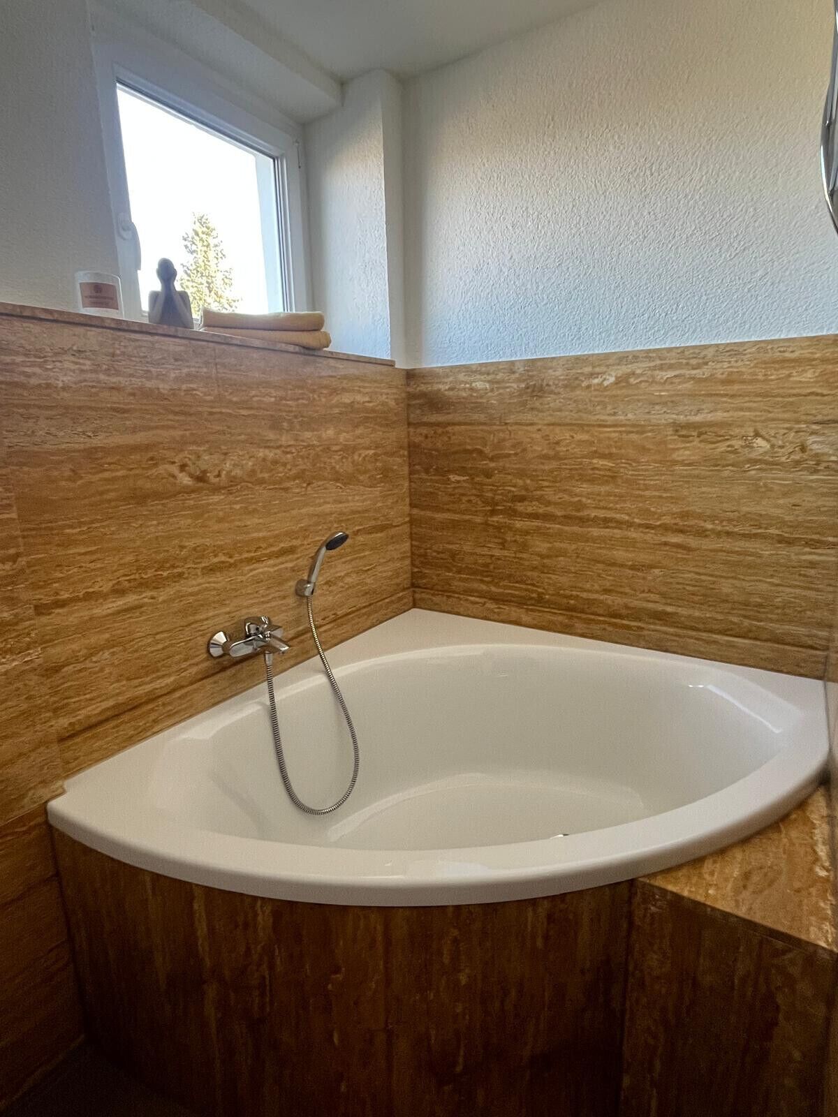 A bathroom with a freestanding bathtub, wooden paneling, and a window above the sink.