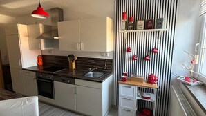 Ett modernt kök med en svart bänkskiva, rostfria vitvaror och en randig vägg med röda muggar.