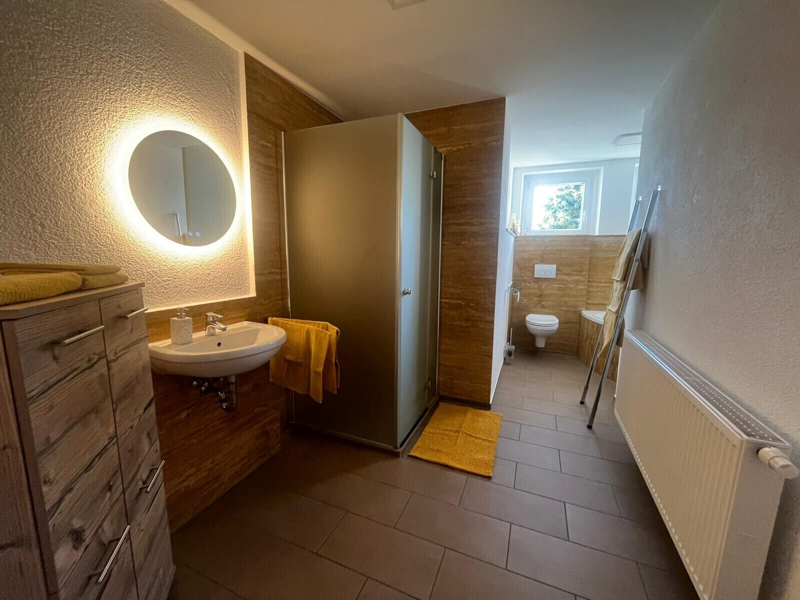 A modern bathroom with a wooden vanity, a round mirror, a sink, and a toilet.