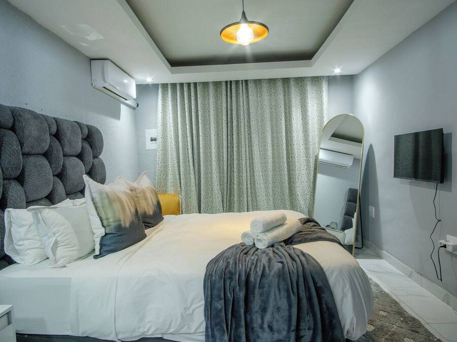 Quarto de hotel moderno com uma cama grande, televisão de tela plana, iluminação no teto e ar condicionado.