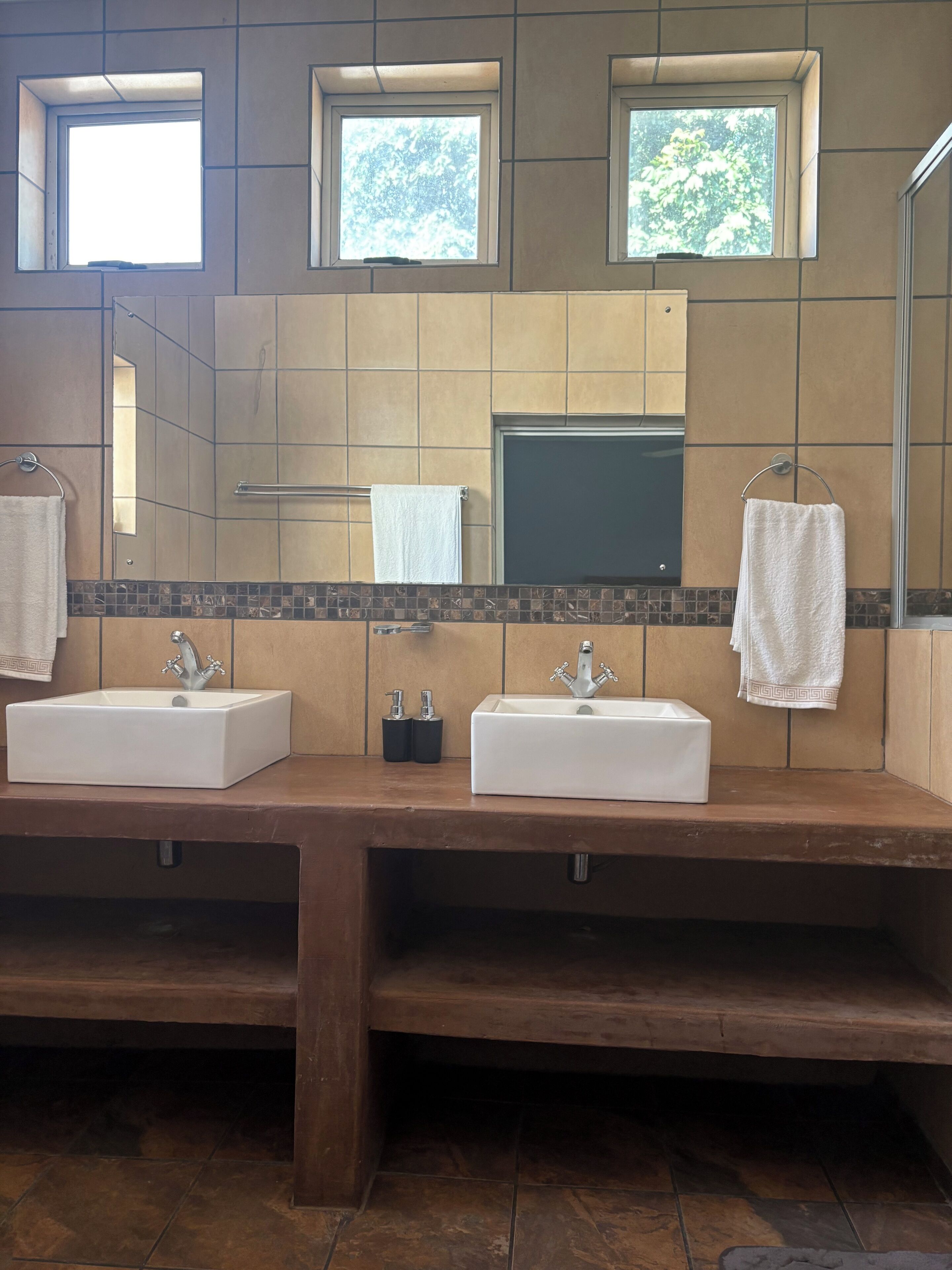 Un baño con dos lavamanos, un espejo y tres ventanas.