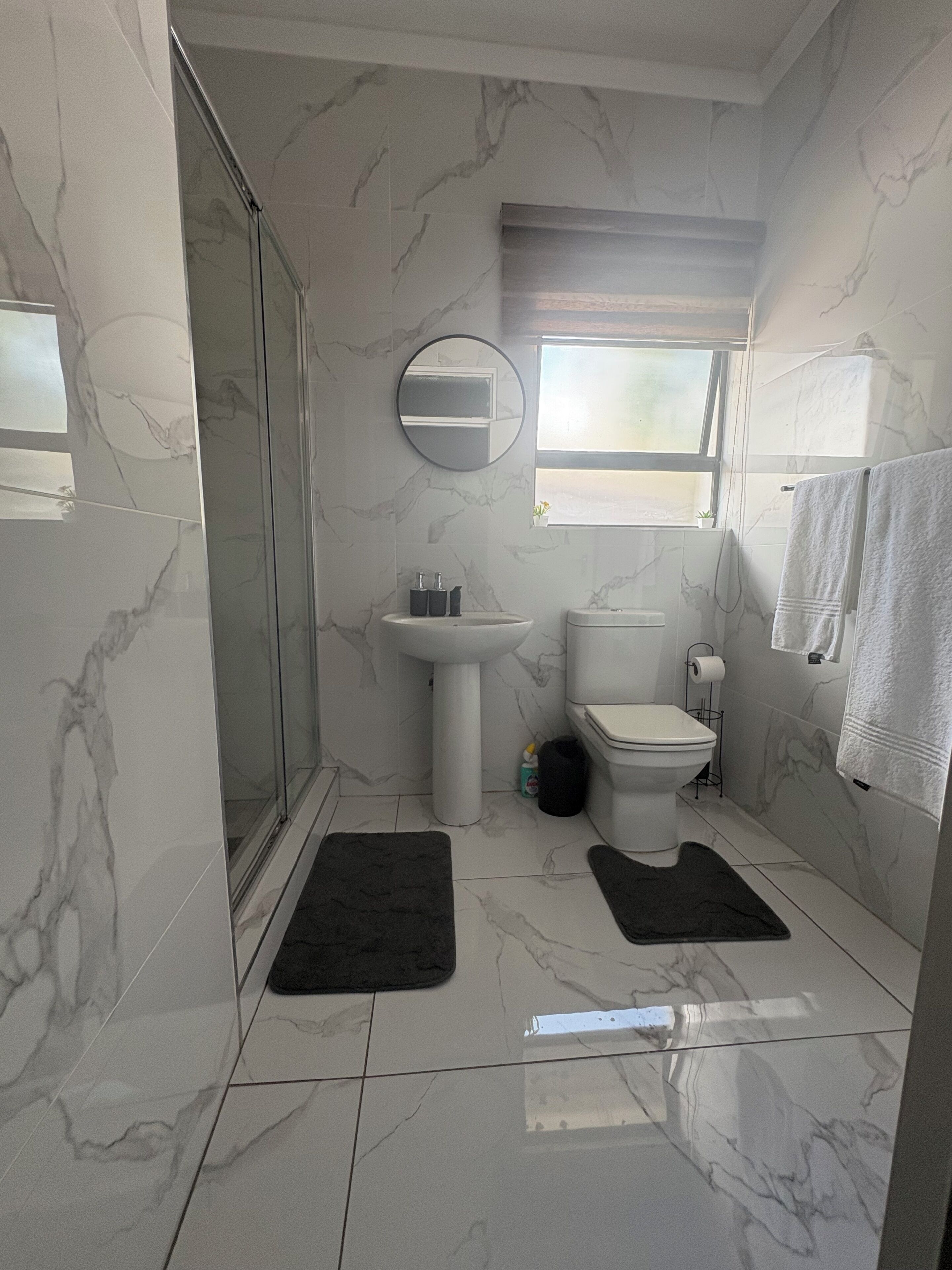 A bathroom with a shower, sink, toilet, and a window.