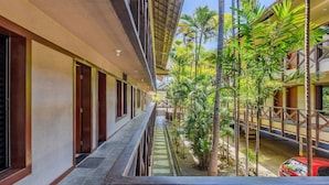 A corridor with a balcony, palm trees, and a red car parked outside. - Eco Paradise #101 - Apt in Cumbuco by Carpediem (Caucaia)