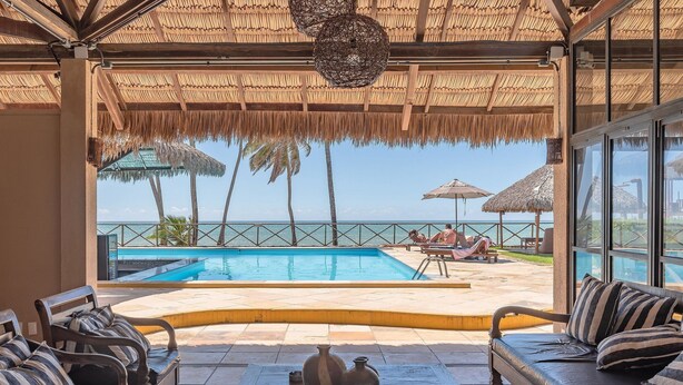 A poolside area with a view of the ocean, a thatched roof, and outdoor furniture. - Eco Paradise #101 - Apt in Cumbuco by Carpediem (Caucaia)