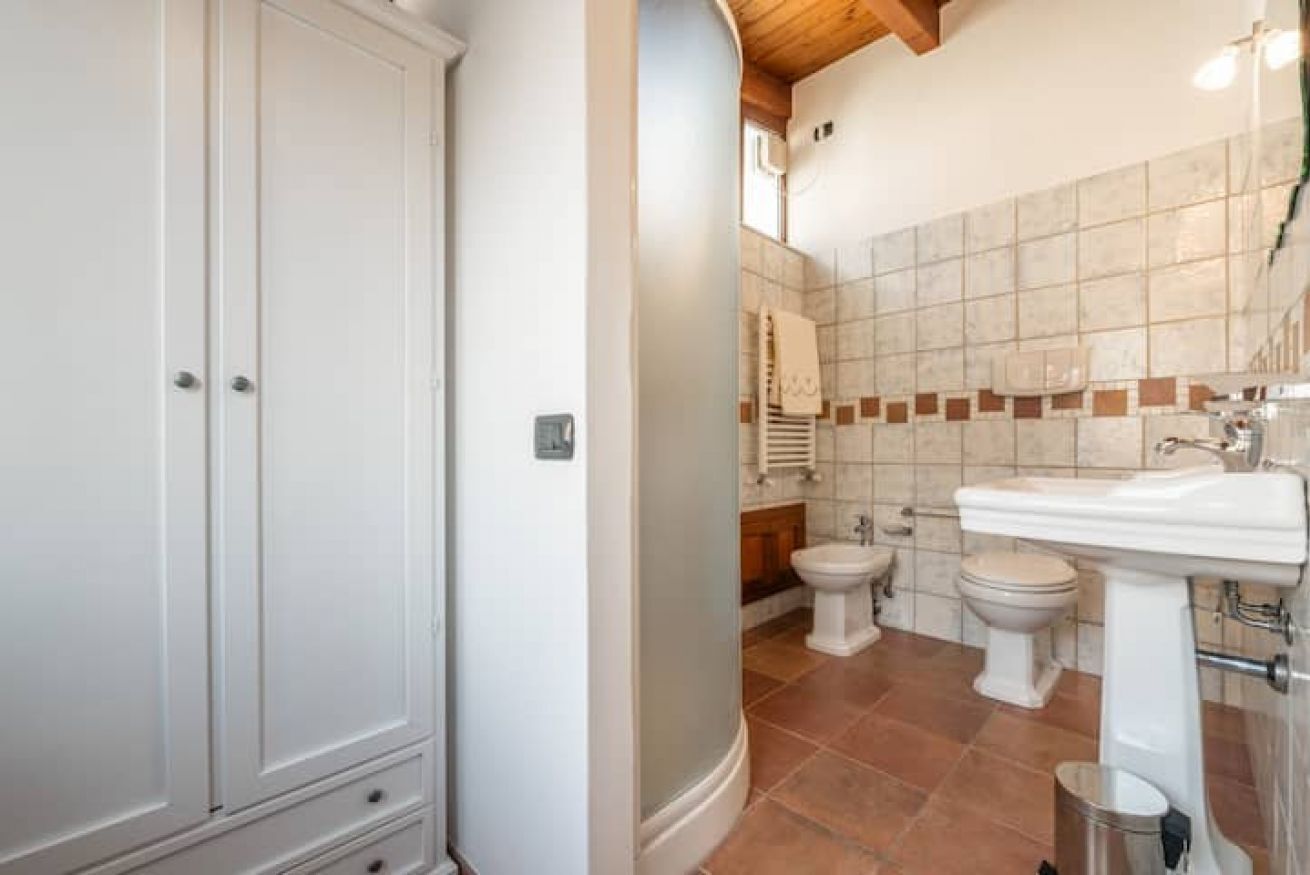 A bathroom with a white cabinet, a sink, and two toilets.