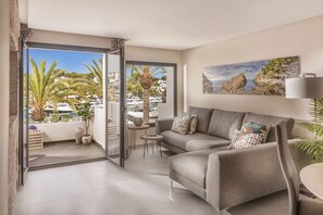 Een moderne woonkamer met een bank, een kleine ronde tafel en een balkon met uitzicht op boten en palmbomen.
