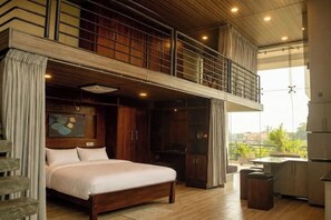 A spacious bedroom with a large bed, wooden flooring, a balcony, and a view of the city. - Modern Open-Plan Loft for 5 in the Heart of Point Pedro (Point Pedro)