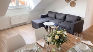 Una sala de estar moderna con un sofá modular gris, una mesa de comedor con platos, vasos y un florero.