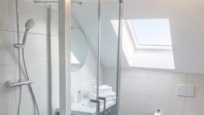 Un baño moderno con ducha de vidrio, tragaluz, lavabo blanco y retrete.