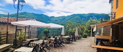 Une terrasse extérieure avec des tables et des chaises, un baby-foot et une vue sur des collines verdoyantes.