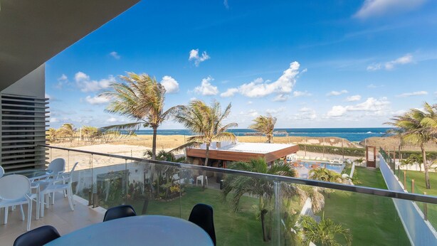 A balcony with a glass railing overlooking a beach, palm trees, and a pool area. - Luxo a Beira Mar - Mansao Exclusiva por Carpediem (Extremoz)