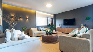 A modern living room with a sofa, armchair, and round coffee table. There is a TV mounted on the wall and a window providing natural light. - Luxo a Beira Mar - Mansao Exclusiva por Carpediem (Extremoz)