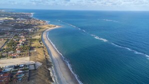 An aerial view of a coastal area with a long sandy beach, a small town with houses and buildings, and the ocean extending to the horizon. - Luxo a Beira Mar - Mansao Exclusiva por Carpediem (Extremoz)