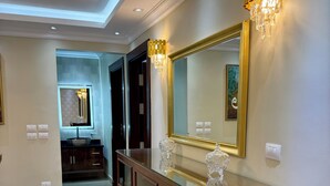 A modern bathroom with a wooden vanity, a large mirror, and a chandelier. - Royal Gameat Al Dewal Residence (Giza Governorate)