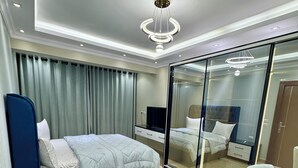 A modern hotel room with a bed, a desk, a chair, a TV, and a large mirror. - Royal Gameat Al Dewal Residence (Giza Governorate)