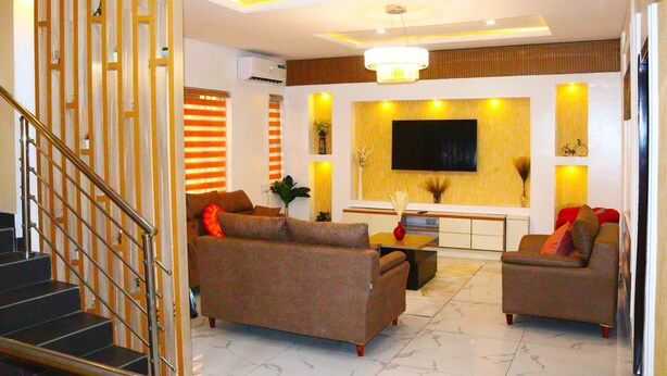 Una sala de estar moderna con escalera, sofás, televisor y candelabro.