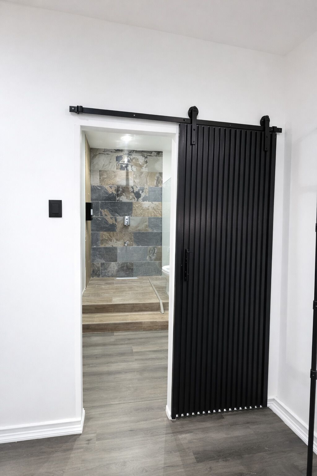 Ein modernes Interieur mit einer Schiebetür zu einem Badezimmer mit gefliestem Duschbereich und einer Marmor-Spritzschutzwand.