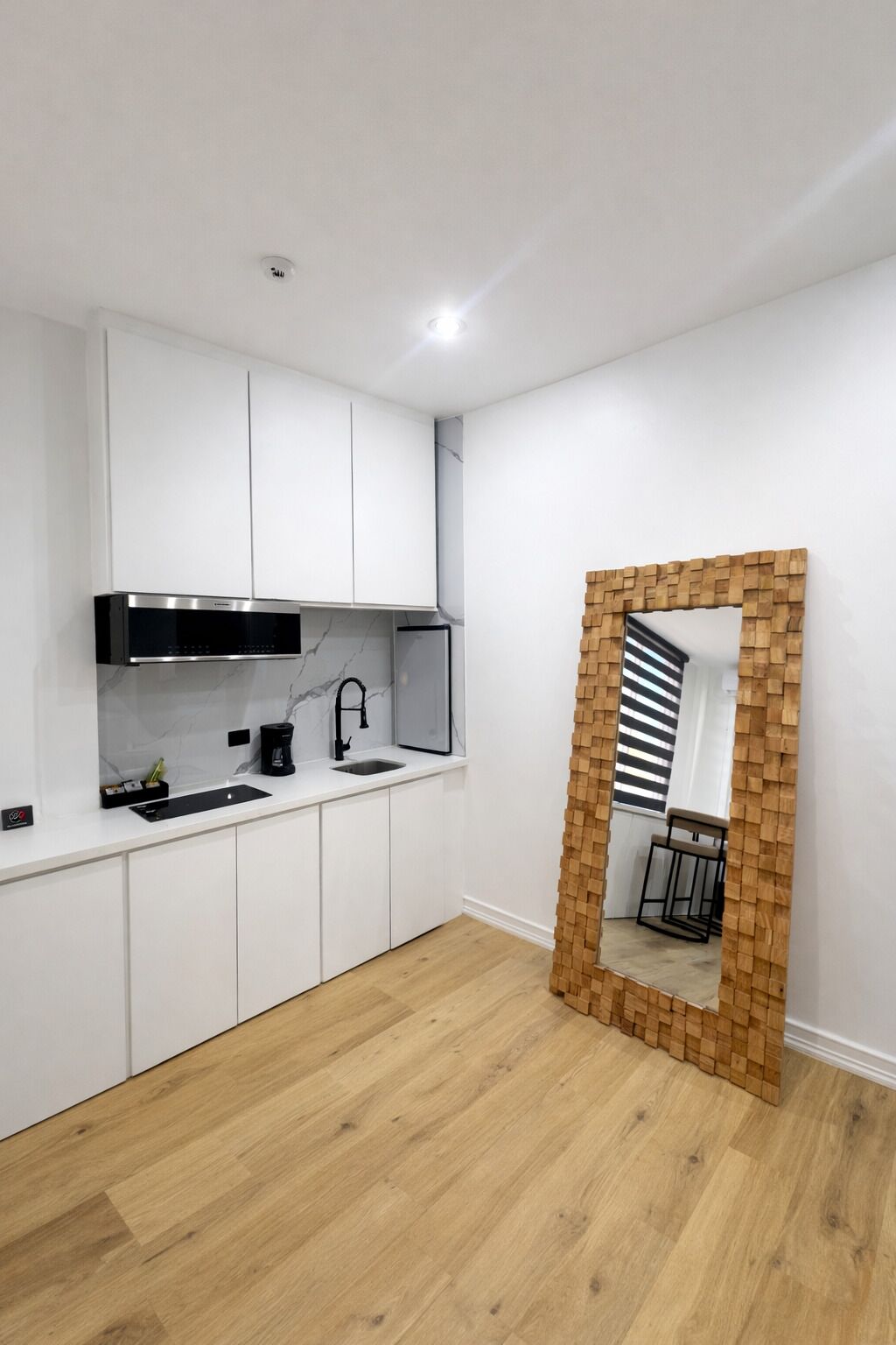 A modern kitchen with white cabinetry, a built-in stove, and a wooden-framed mirror.
