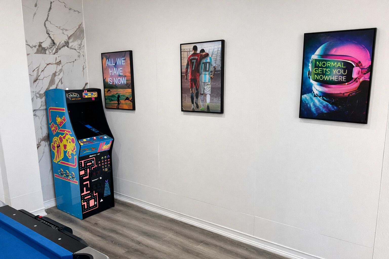 A room with a foosball table, a claw machine, and three framed posters on the wall.