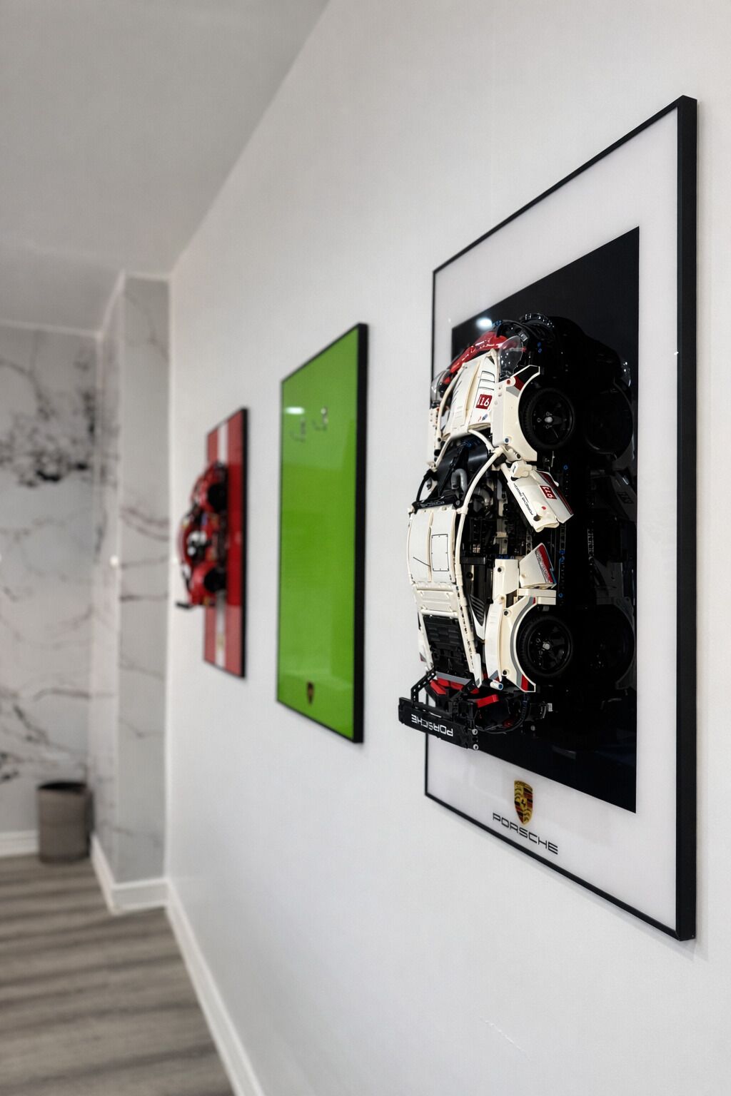 A hallway with framed artwork on the wall, a marble floor, and a staircase in the background.