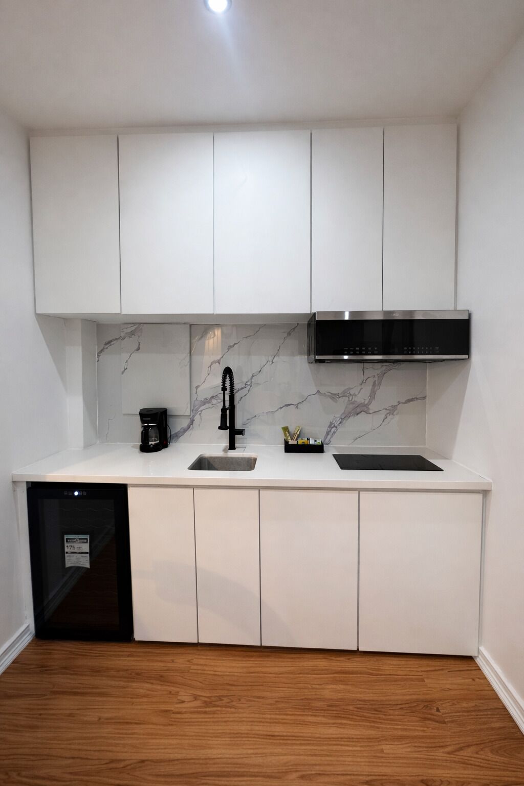 A compact kitchen with white cabinets, a black faucet, a built-in microwave, and a dishwasher.