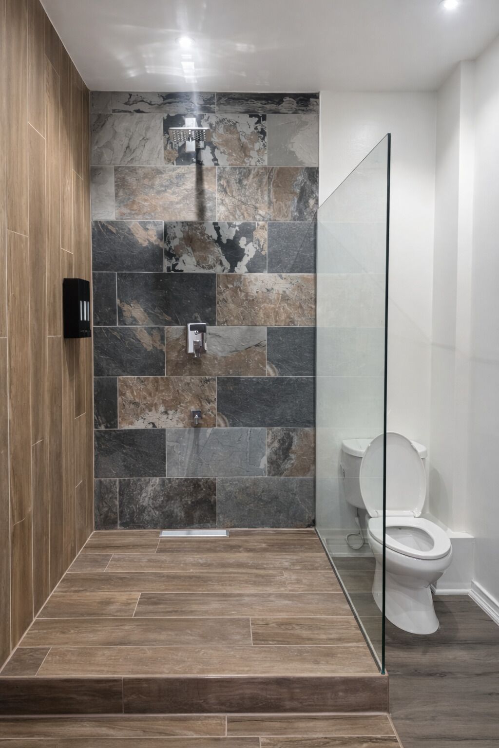 Un baño moderno con ducha, paredes de azulejos y un inodoro.