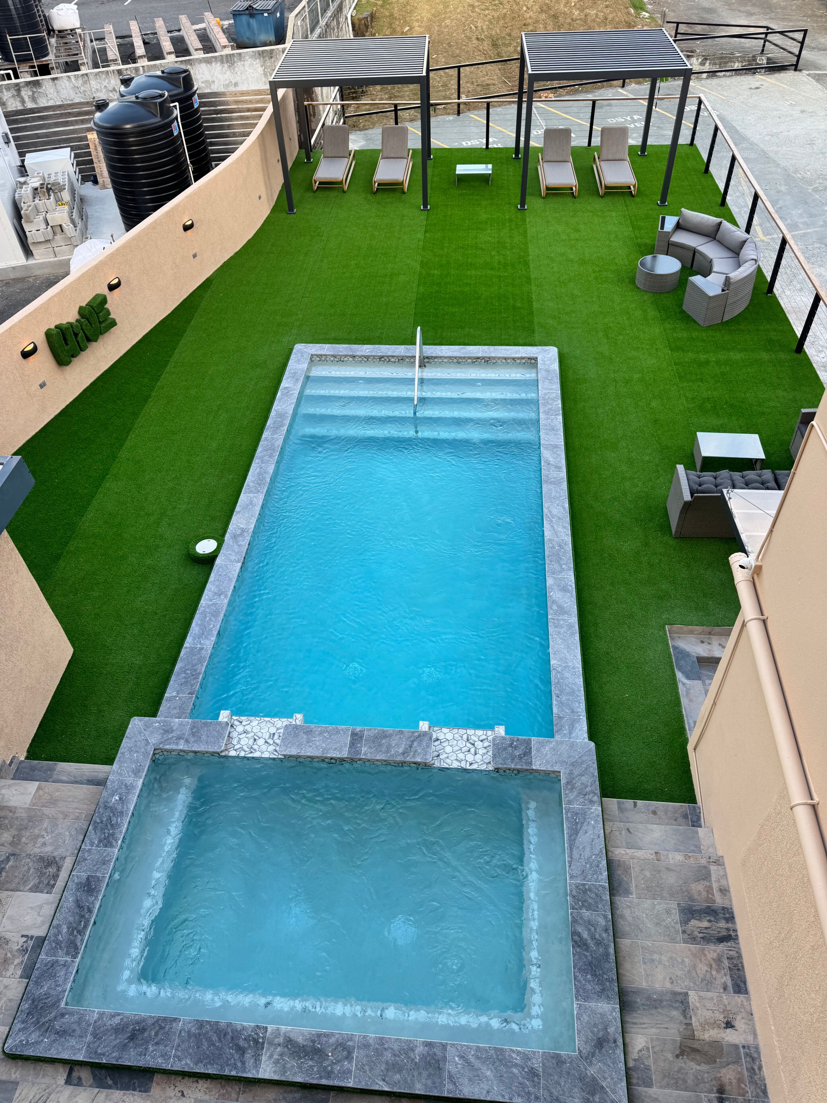 Une piscine rectangulaire entourée d’une pelouse artificielle verte, un petit jacuzzi et un espace salon extérieur.
