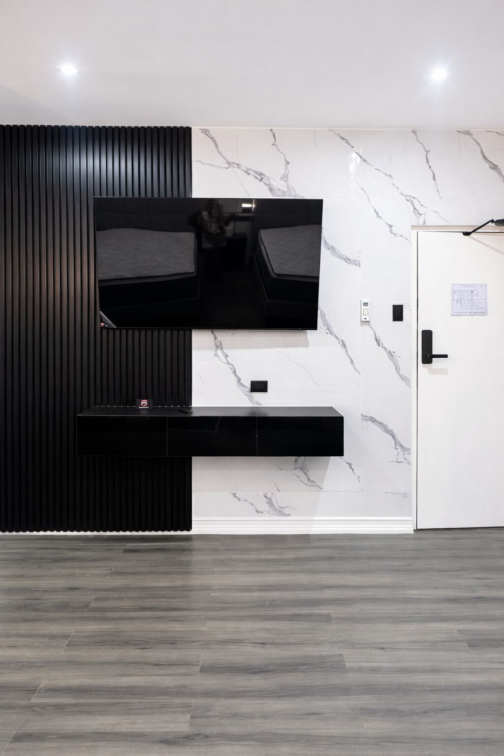 A modern room with a TV mounted on a wall, a black console table, and a marble-patterned wall.