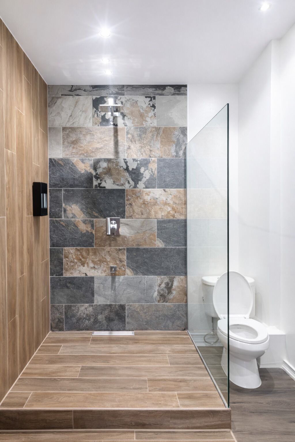 A modern bathroom with a shower, a toilet, and a wooden floor.