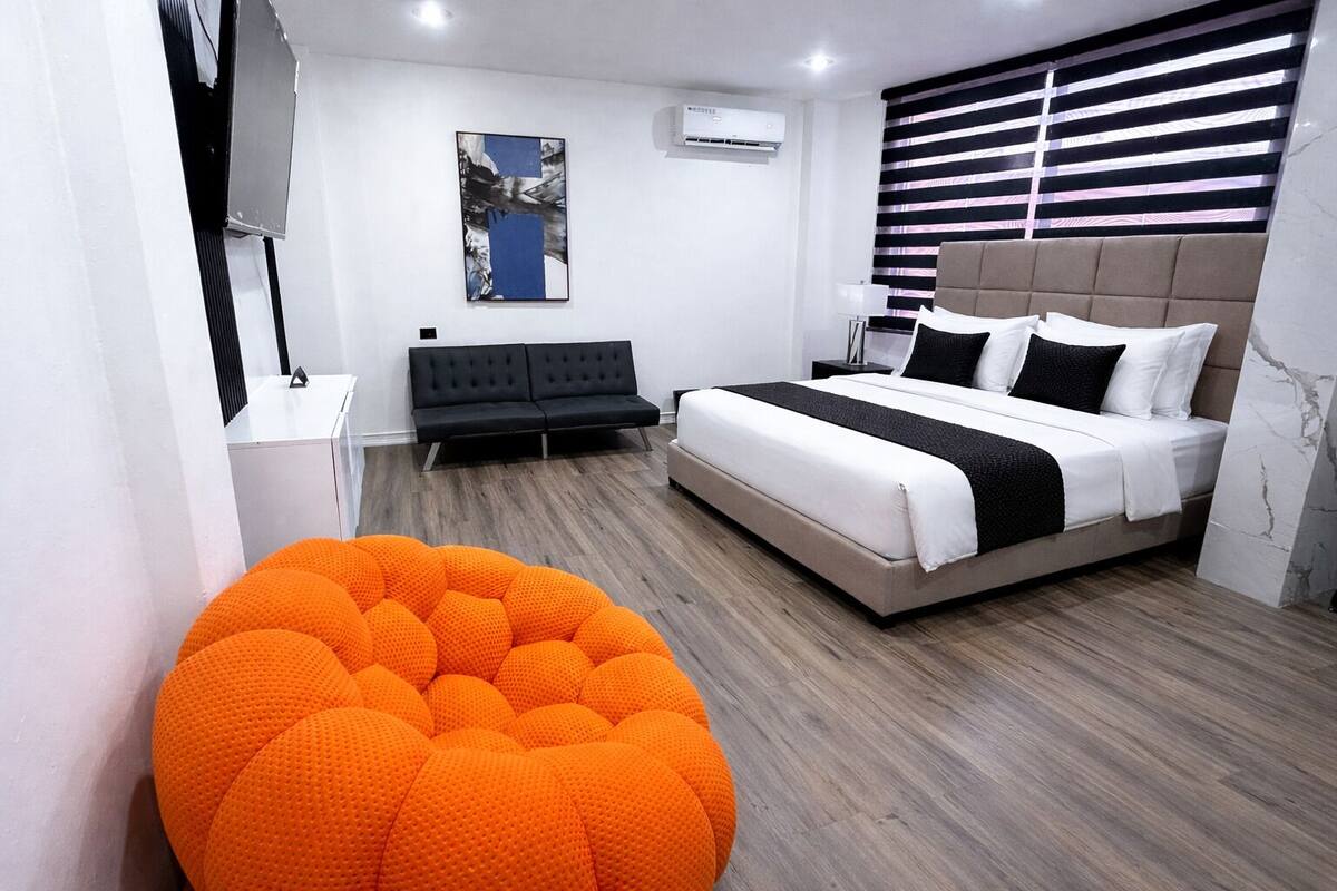 A modern bedroom with a bed, a sofa, a bean bag chair, and a painting on the wall.
