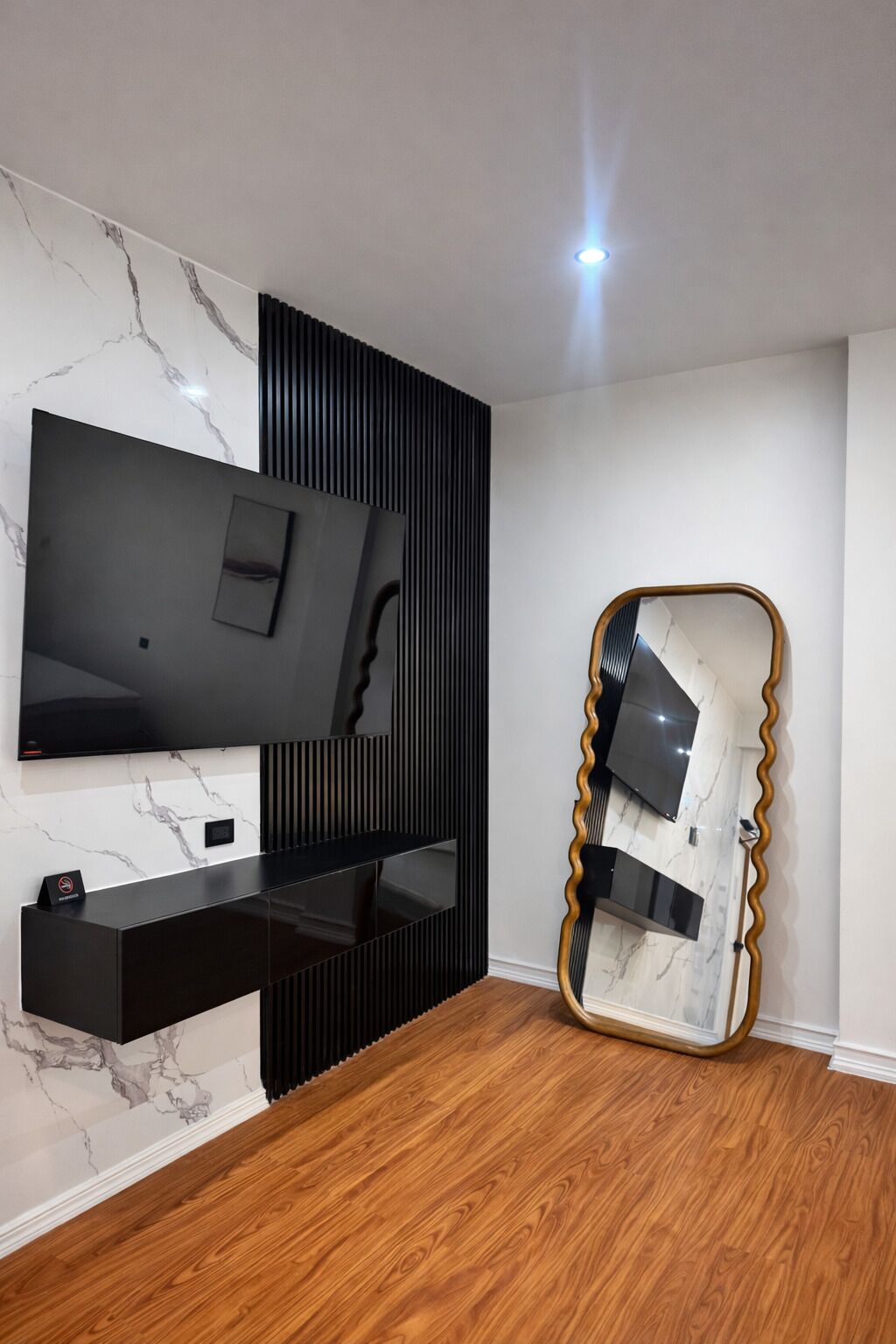 A modern living room with a flat-screen TV, black entertainment unit, and a unique wavy mirror.