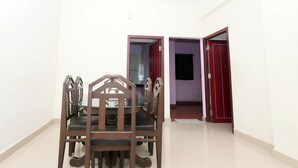 A dining area with a wooden table and chairs, a red door, and a white wall. - Sanjana The Luxurious Family Stay 1 (Karkala)
