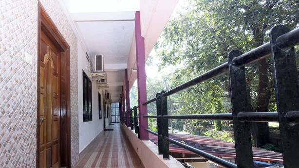A corridor with a tiled floor, a wooden door, and a balcony with a metal railing. - Sanjana The Luxurious Family Stay 1 (Karkala)