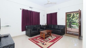A living room with two black sofas, a wooden coffee table, and a red and beige patterned rug. - Sanjana The Luxurious Family Stay 1 (Karkala)