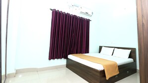 A bedroom with a bed, a window with purple curtains, and an air conditioning unit. - Sanjana The Luxurious Family Stay 1 (Karkala)