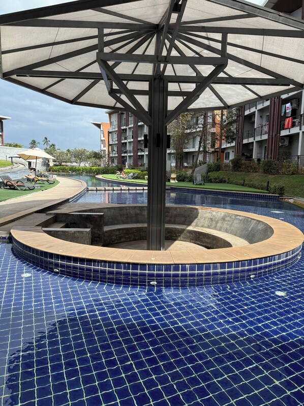 A swimming pool with a tiled deck, a central water feature, and a covered seating area. - Charming 1-bedroom Apartment Near Bangrak Beach (Koh Samui)