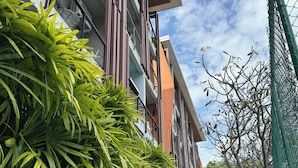 A modern building with balconies, a concrete planter with green foliage, and a clear sky. - Charming 1-bedroom Apartment Near Bangrak Beach (Koh Samui)