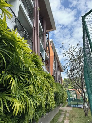 A modern building with balconies, a concrete planter with green foliage, and a clear sky. - Charming 1-bedroom Apartment Near Bangrak Beach (Koh Samui)