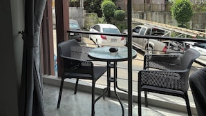 A balcony with two chairs and a small table, overlooking a street with parked cars and buildings. - Charming 1-bedroom Apartment Near Bangrak Beach (Koh Samui)