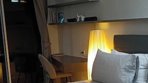 A hotel room with a large bed, a desk, and a chair. There is a lamp on the desk and a curtain on the window. - Charming 1-bedroom Apartment Near Bangrak Beach (Koh Samui)