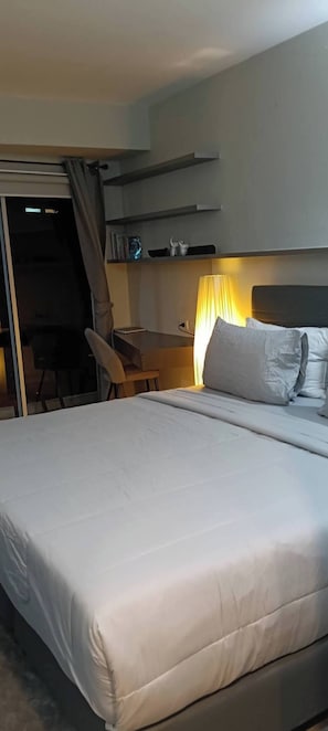 A hotel room with a large bed, a desk, and a chair. There is a lamp on the desk and a curtain on the window. - Charming 1-bedroom Apartment Near Bangrak Beach (Koh Samui)